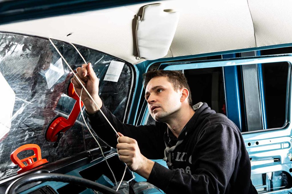 Sebastian zieht die neue Frontscheibe bei unserem VW Bus T2 Marktwagen Toni ein.